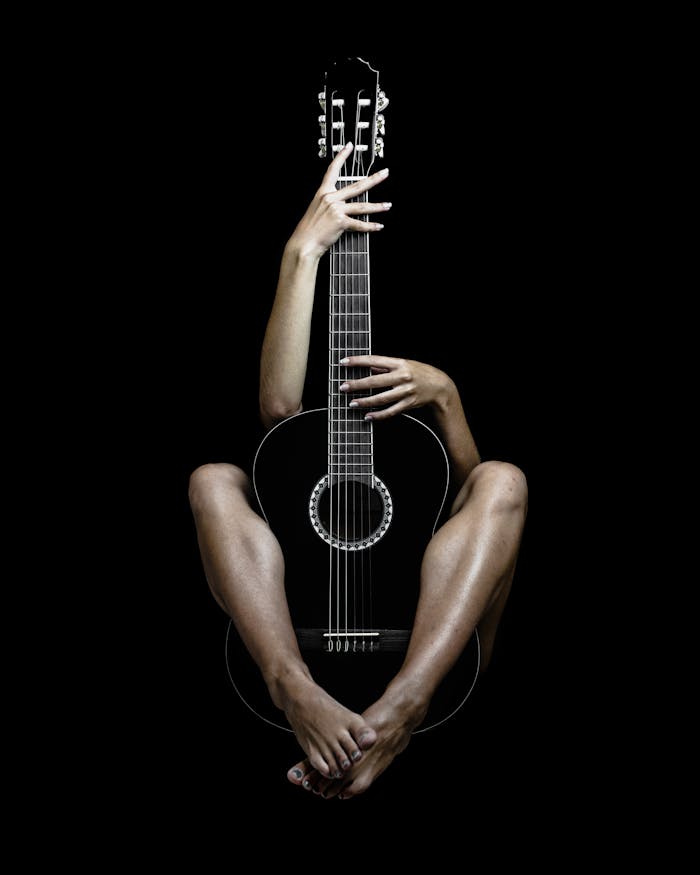 Conceptual image of feet and hands embracing a guitar against a black background.