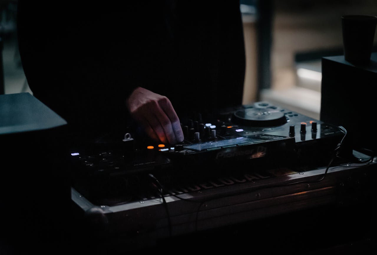 A DJ adjusting a mixer in a dimly lit venue, creating an energetic atmosphere.